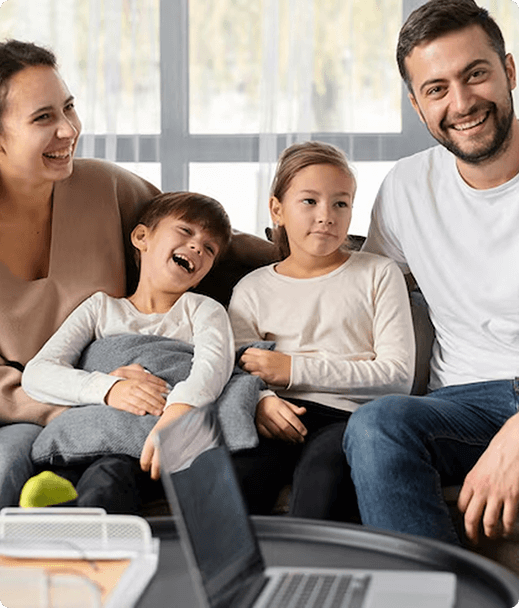 Family enjoying time together at home, smiling and laughing, with a laptop and a cozy atmosphere, reflecting the importance of health insurance for personal and family well-being.